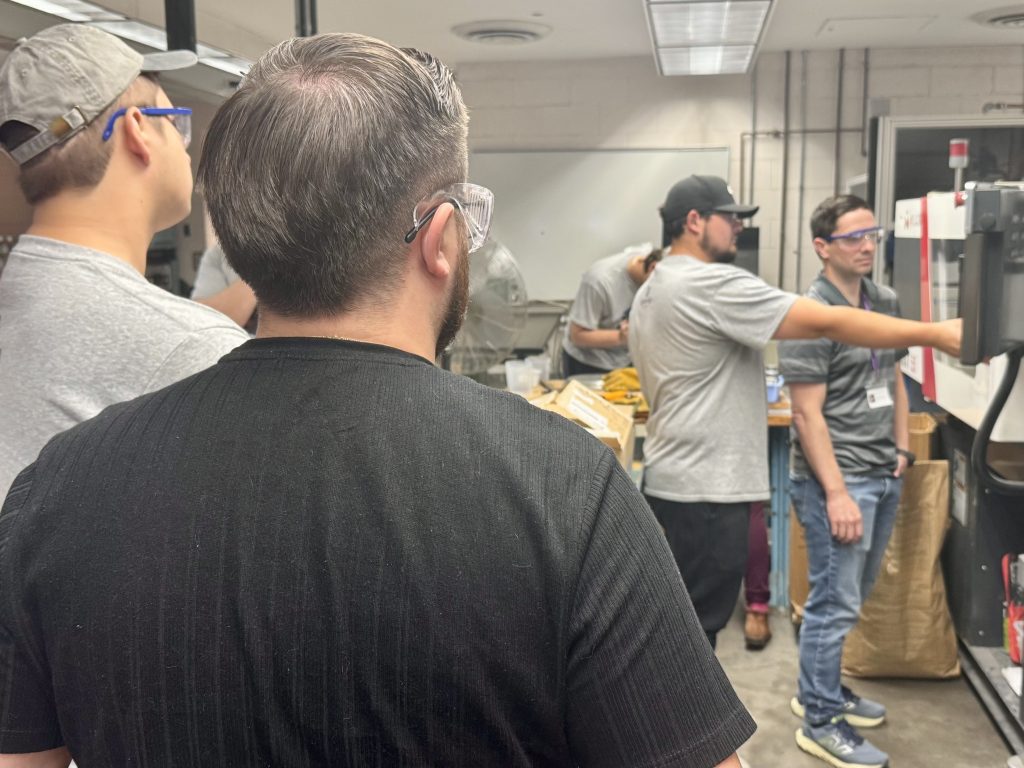 Joe watches Matt as he works on the injection molding machine