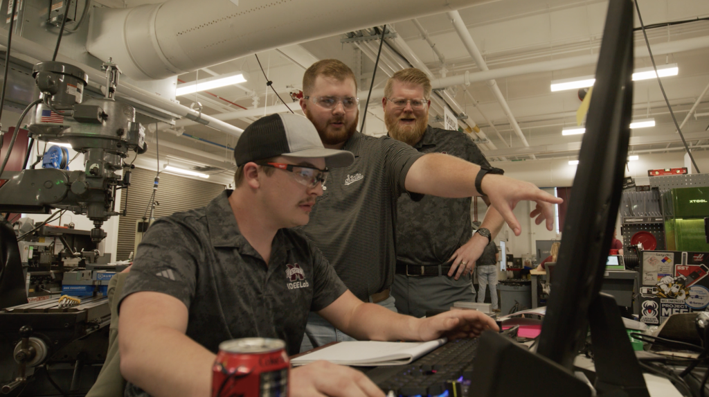 Collin Mullins works on a computer with others looking on